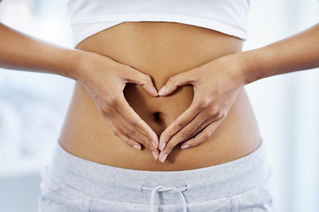 A woman forming a heart with her hands, around her stomach to show her gut is happy and feels good.