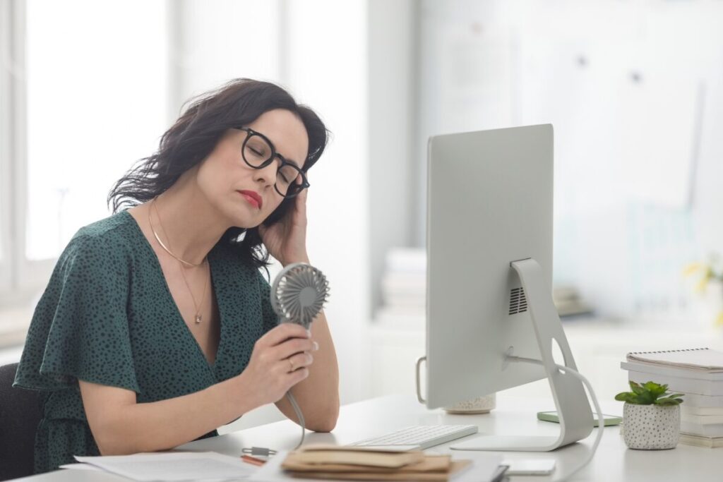 A woman holding a mini fan, dealing with hot flashes.