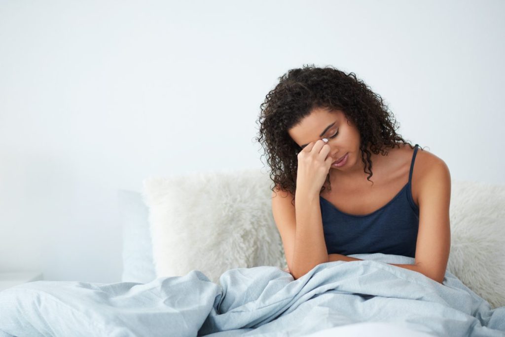 A woman in bed, hand holding between her eyes, tired and frustrated.