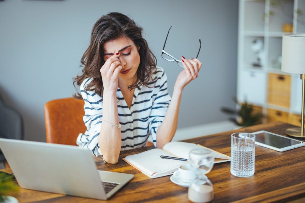 A lady with her hand to her face, trying to work but clearly feeling stressed.