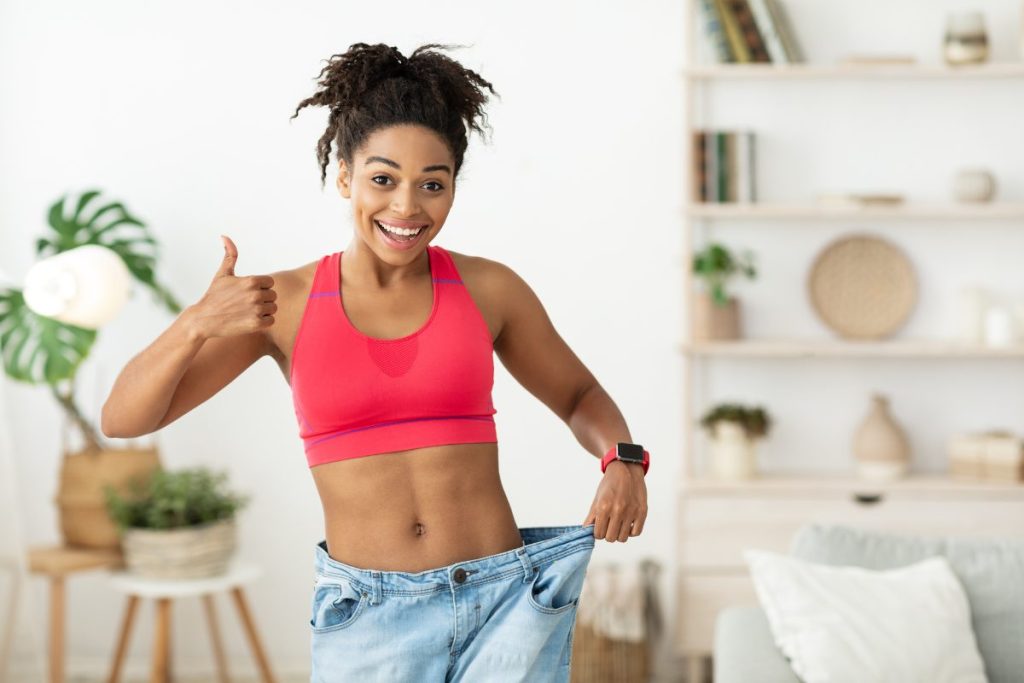 A woman holding up her bigger jeans that no longer fit her, with a thumbs up.