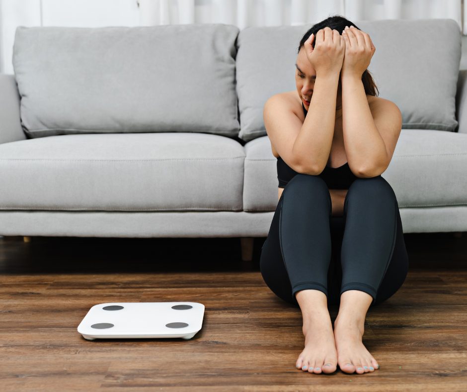 Woman in her 40s feeling tired and frustrated next to a scale, showing difficulty with weight after.